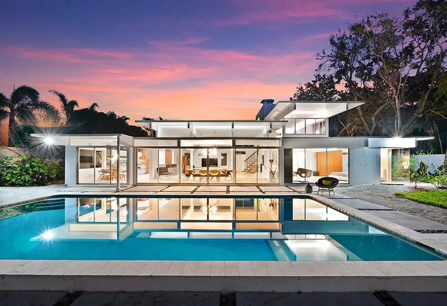 Mid century modern home staging in Lido Shores Sarasota featuring glass architecture, pool reflection, and indoor outdoor living at sunset
