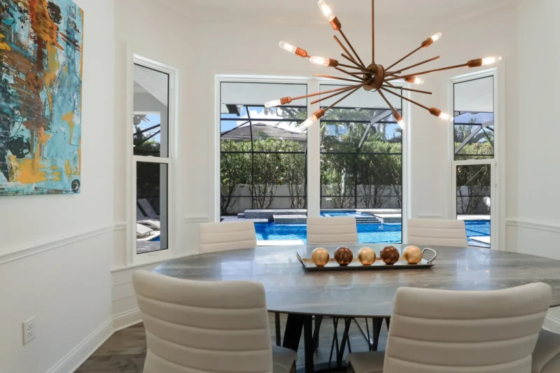 Modern coastal dining room staging with designer chandelier overlooking pool in West of Trail Sarasota home