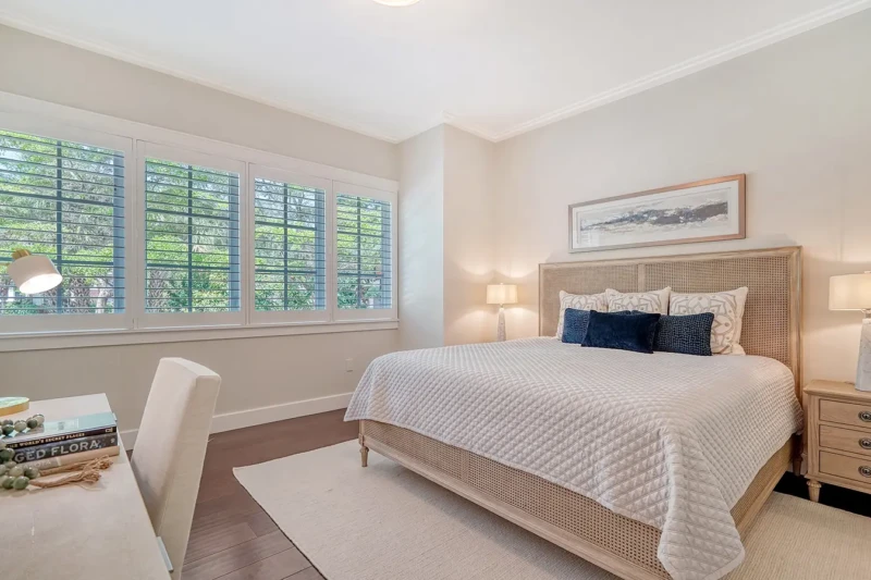 Coastal guest bedroom staging with neutral furnishings and plantation shutters