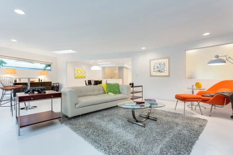 Contemporary living room staging in Bird Key Sarasota with minimalist white interiors, orange lounge chair, and modern furnishings