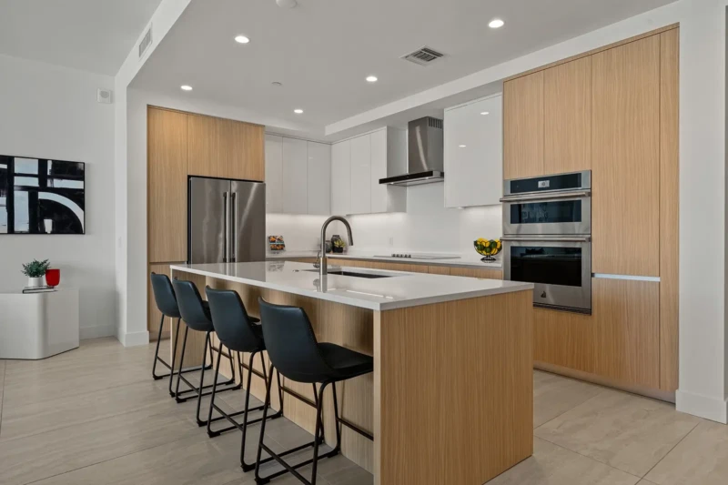 Luxury condo kitchen home staging with contemporary wood cabinetry, oversized waterfall island, and modern bar seating in Sarasota residence