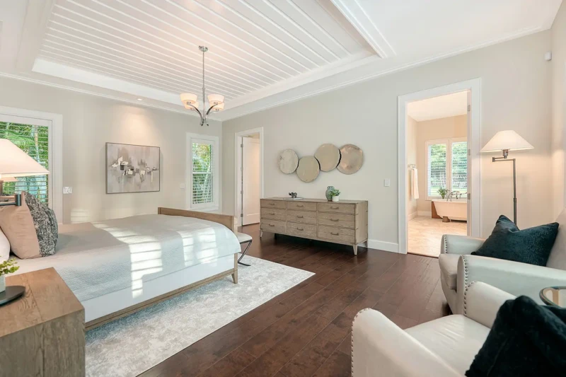 Luxury primary suite staging with coastal contemporary furnishings and warm wood flooring