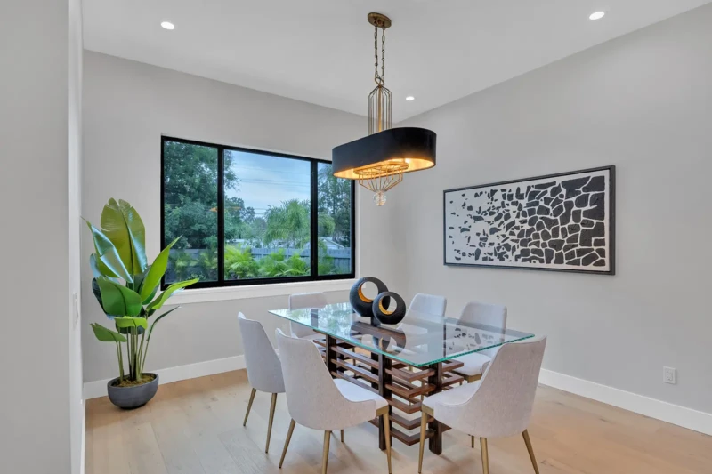 Modern dining room staging in East of the Trail Sarasota home featuring a glass dining table, contemporary lighting fixture, and minimalist luxury interior design accents