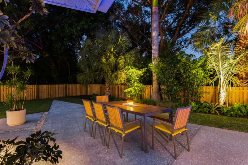 Modern outdoor patio staging in Bird Key Sarasota with teak dining set, tropical landscaping, and evening landscape lighting
