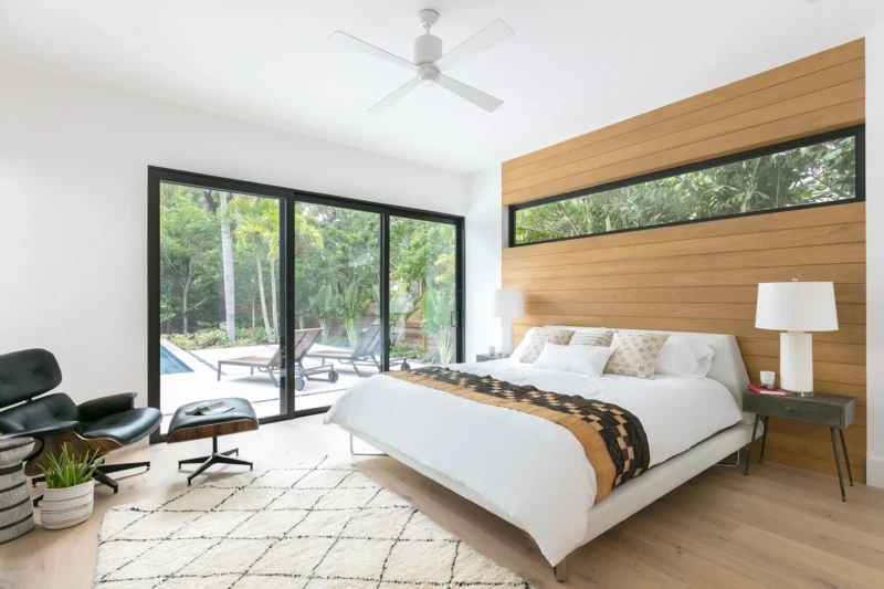 Modern primary bedroom home staging in Sarasota featuring warm wood accent walls, floor-to-ceiling glass, and resort-style indoor-outdoor living