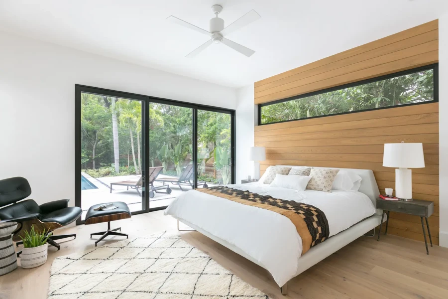 Modern primary bedroom home staging in Sarasota featuring warm wood accent walls, floor-to-ceiling glass, and resort-style indoor-outdoor living