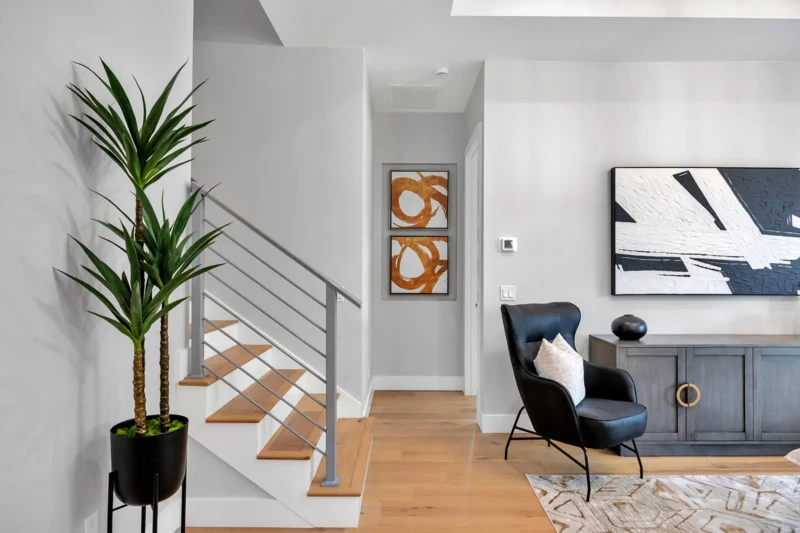 Modern staircase and living room detail in staged East of the Trail Sarasota home featuring contemporary furnishings, warm wood flooring, and minimalist interior design accents