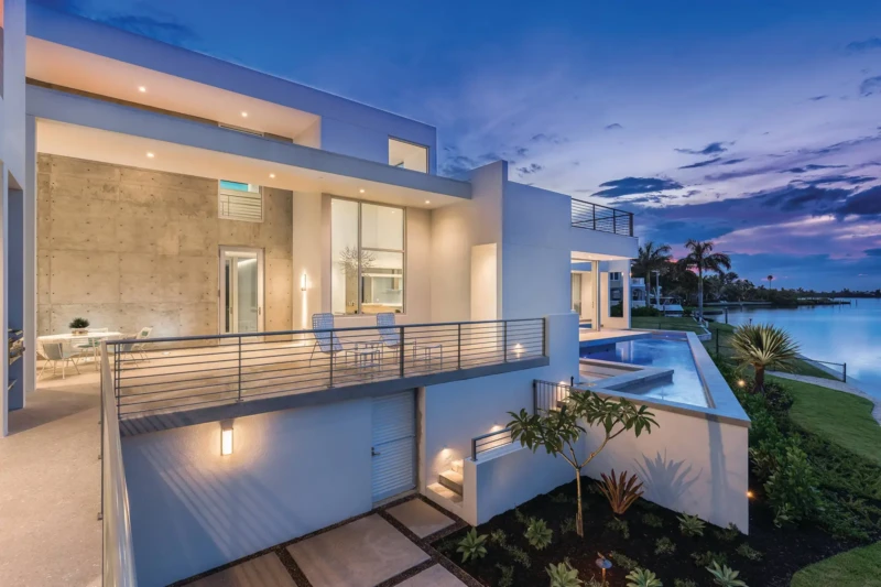 Modern waterfront luxury home exterior at dusk with pool terrace and bay views in Longboat Key