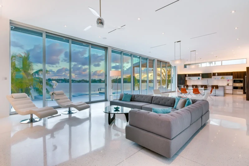 Modern waterfront living room staging in Sarasota with floor-to-ceiling glass walls, open-concept interiors, and luxury contemporary furnishings overlooking the bay at sunset