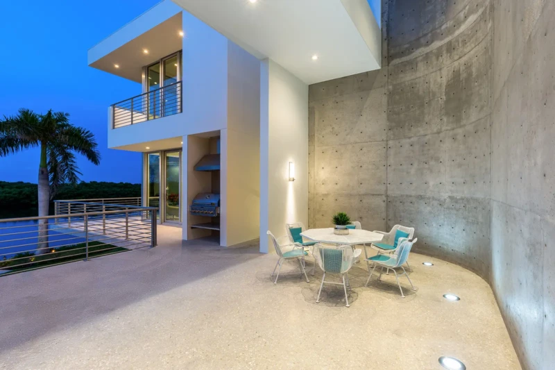 Modern waterfront terrace with curved concrete wall and outdoor dining area in Longboat Key luxury home