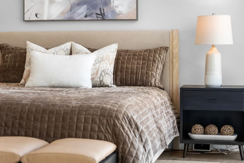 Neutral bedroom home staging with layered bedding, bedside lamp, and modern decor