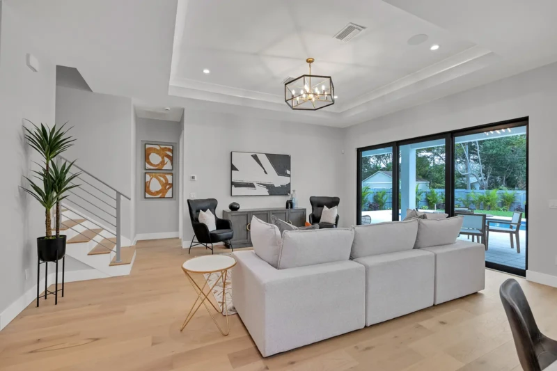 Open-concept living room staging in East of the Trail Sarasota home with modern furnishings, light wood flooring, contemporary staircase, and poolside indoor-outdoor living design