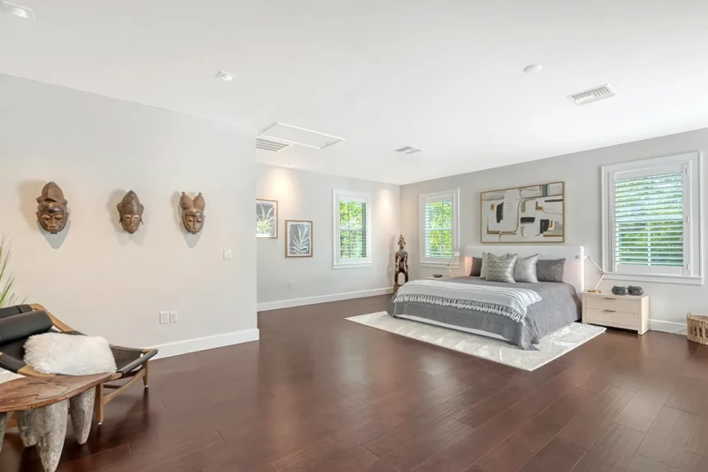 Spacious primary bedroom staging with contemporary coastal furnishings and dark wood floors