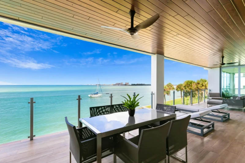 Luxury waterfront outdoor living terrace on Siesta Key with panoramic Gulf views, modern lounge seating, and covered dining area staged for coastal luxury living in Sarasota